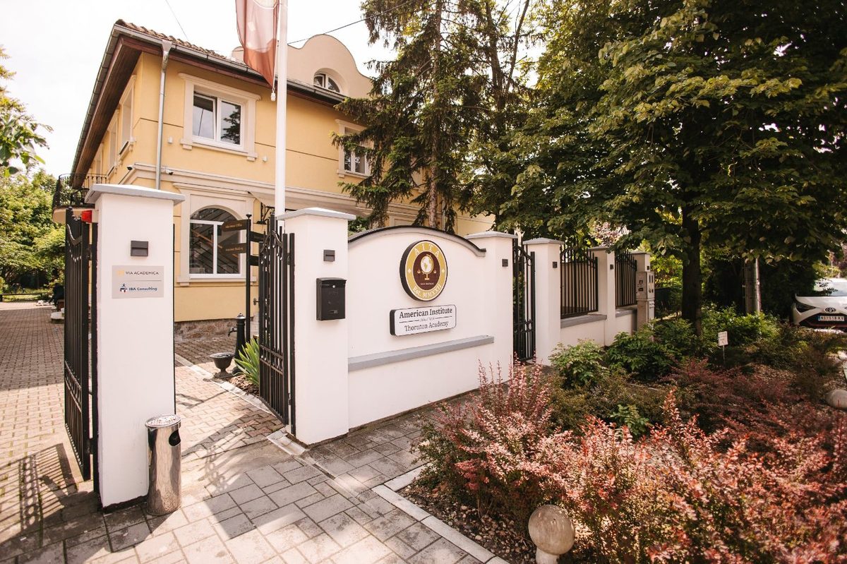 The gate and yellow façade of the American Institute in Novi Sad, with the school sign on the wall