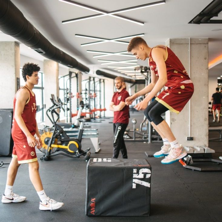 A student in team kit jumping onto a box in the school gym