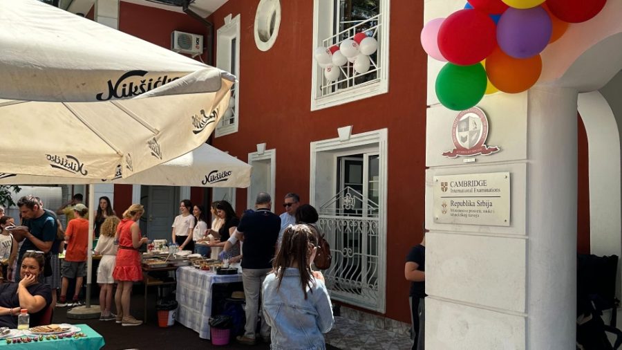 Families and students outside the red campus building on bazaar day, beside the Cambridge International plaque