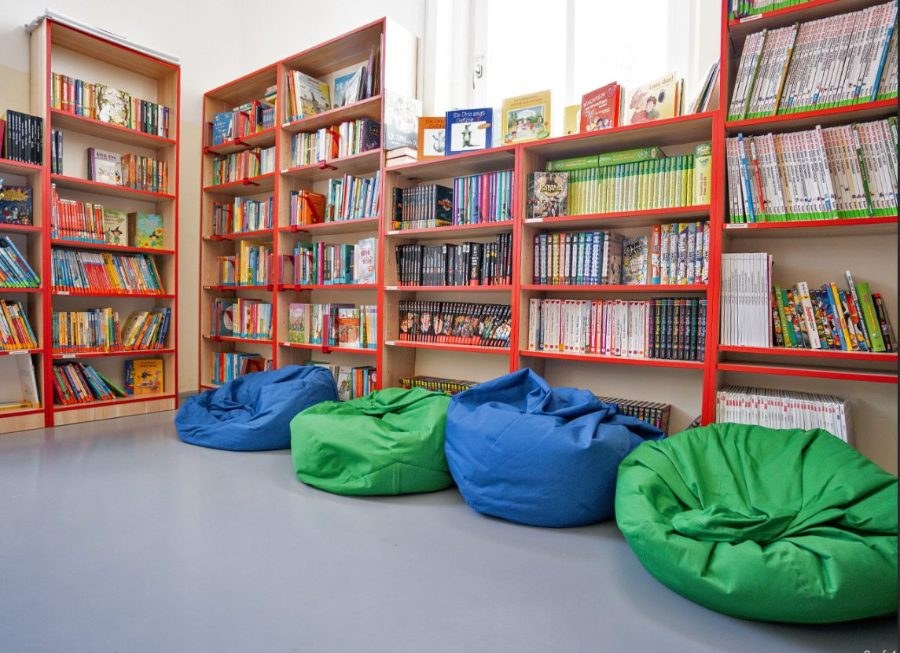 The school library, with red shelves of books along the wall and bean bags on the floor