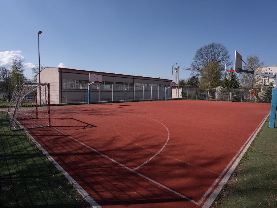 The outdoor sports court with goals and a basketball hoop beside the sports hall