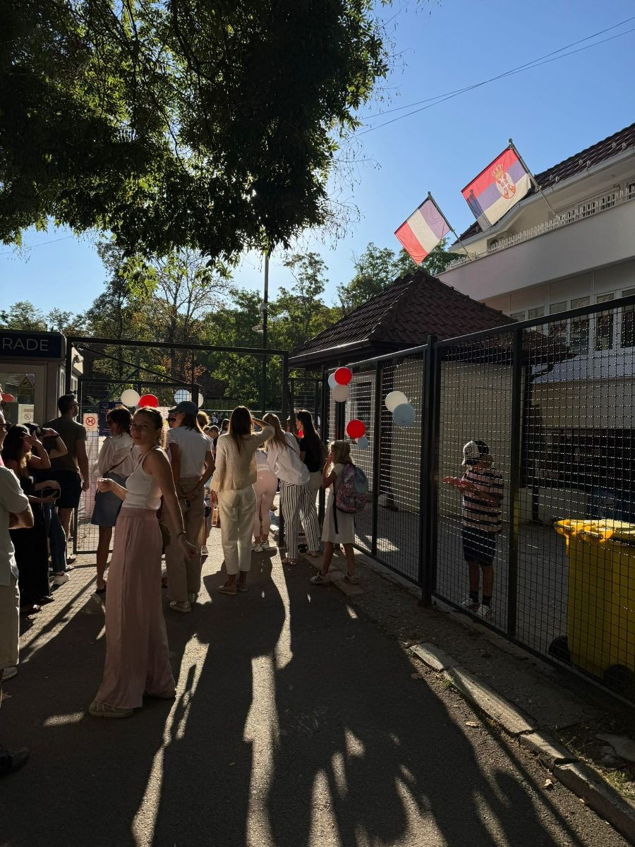 Students walking into the school on a sunny morning, French and Serbian flags above the entrance