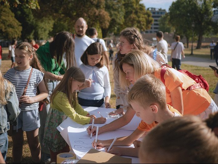 Children and parents drawing together on a long sheet of paper in a park