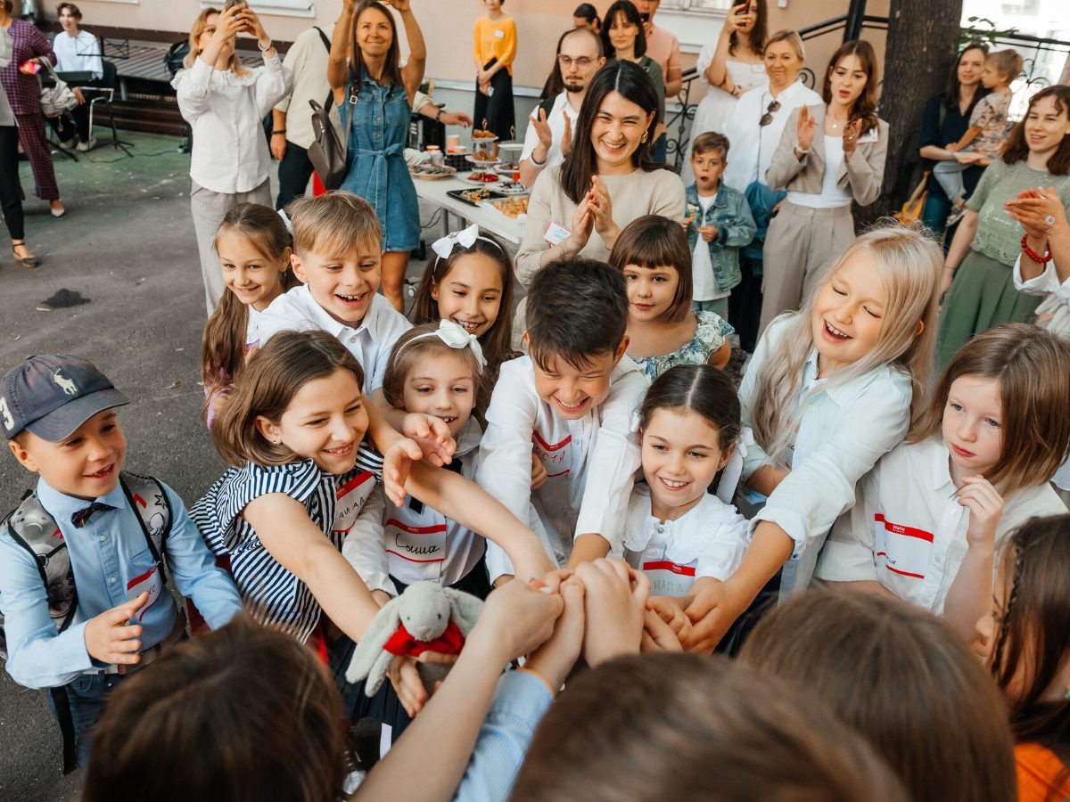 Children join hands in the middle of a circle while parents and teachers clap around them