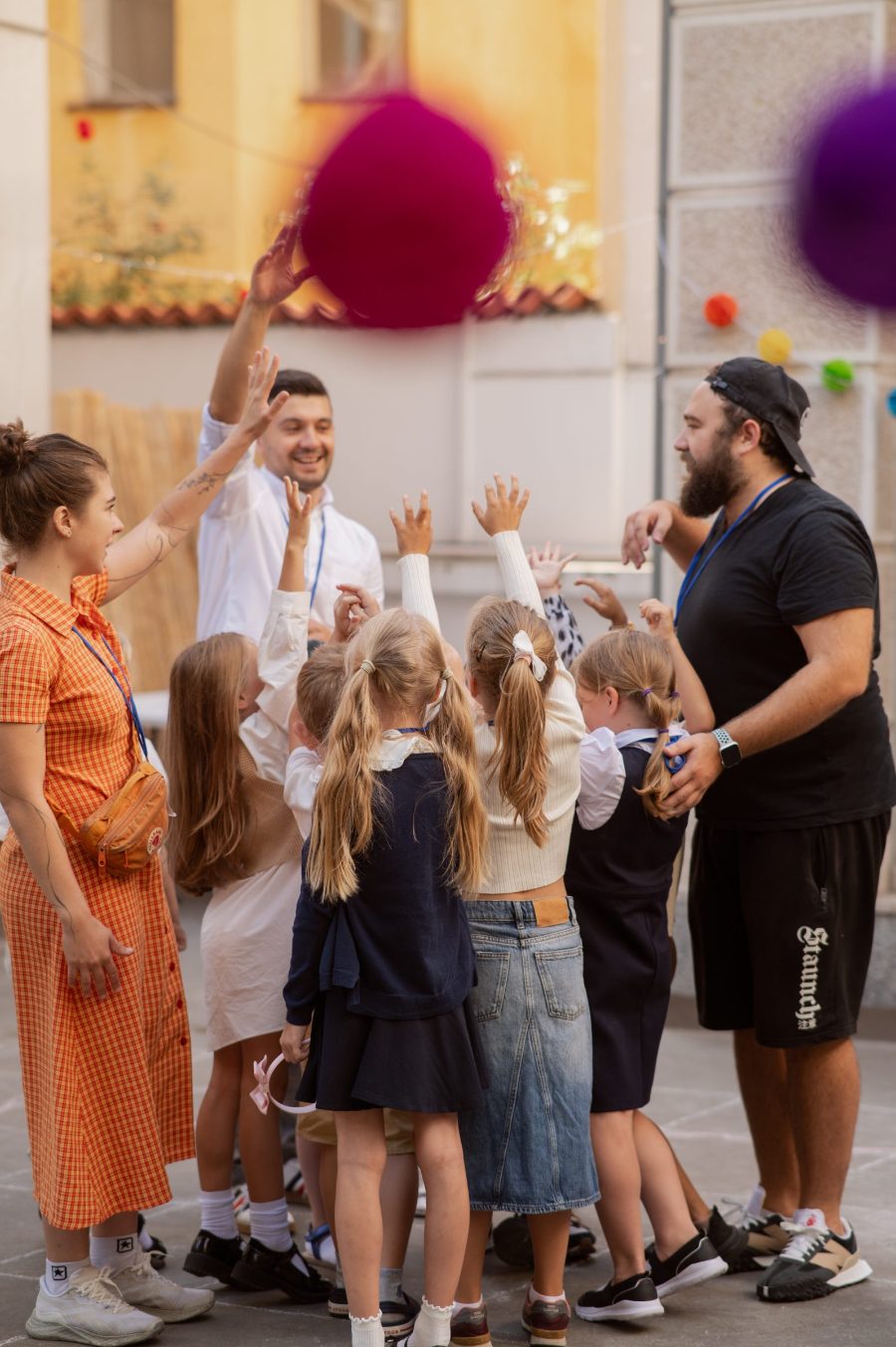 Young pupils reach up for coloured balls tossed by their teachers in the school courtyard
