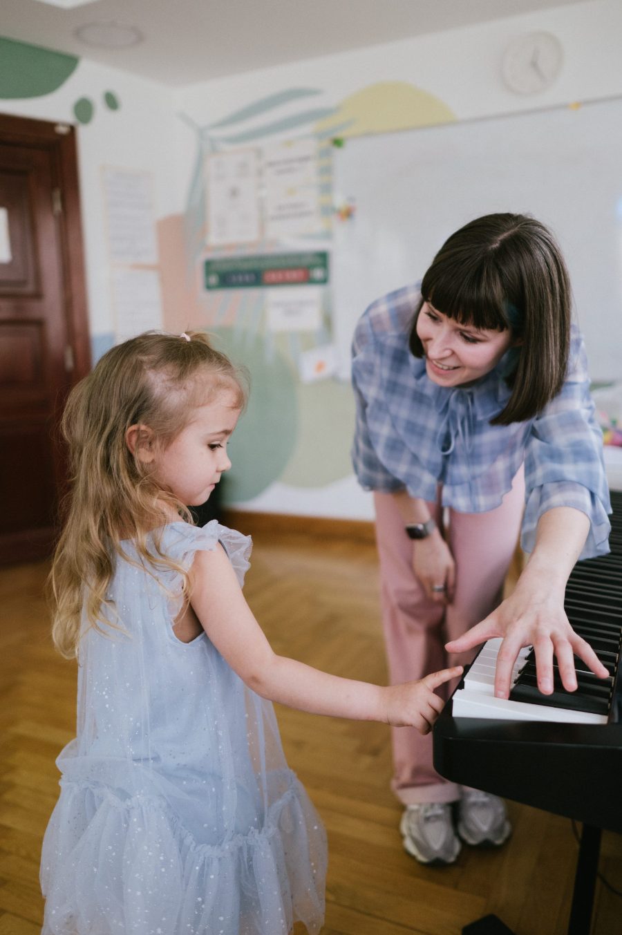 A teacher shows a small girl the keys of an electric piano