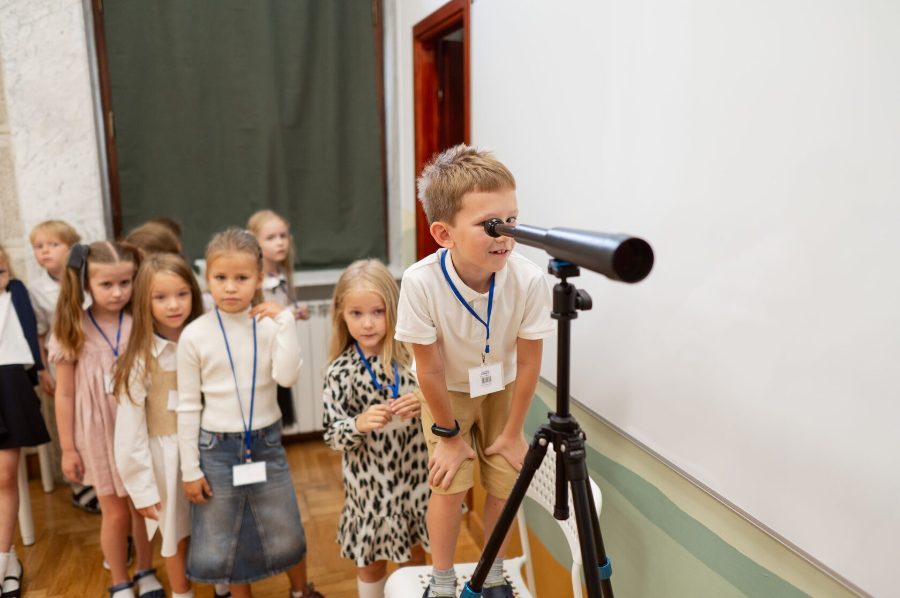 A boy looks through a telescope on a tripod while classmates wait their turn