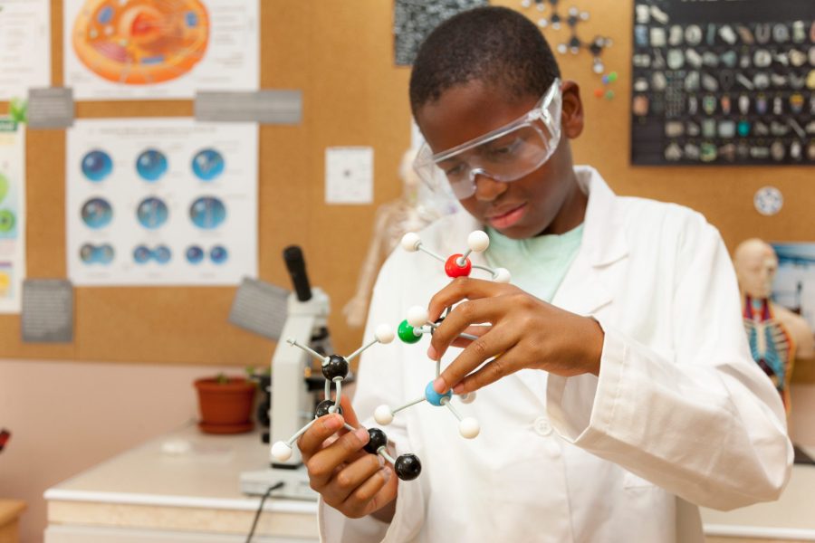 A pupil in safety goggles and a lab coat holding a molecular model in the Science Lab
