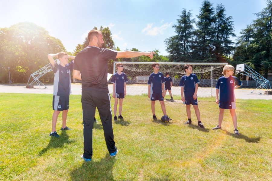 A coach giving instructions to pupils in football kit on the grass pitch